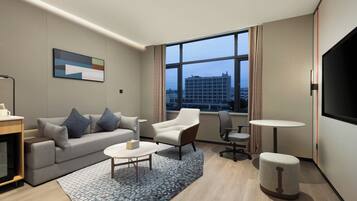 Una habitación de hotel moderna con sofá, sillón, mesa de centro y televisor.