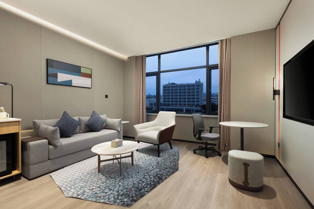 Een moderne hotelkamer met een bank, fauteuil, salontafel en een televisie.