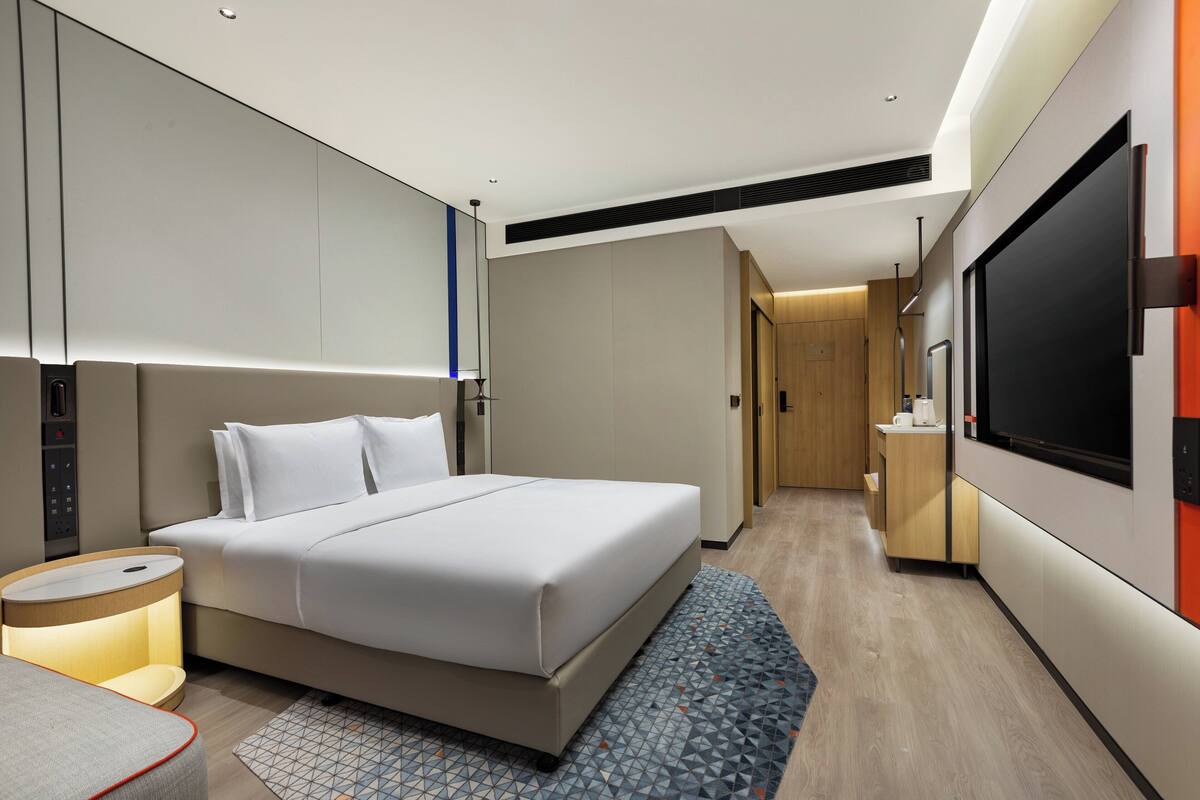 Een moderne hotelkamer met een groot bed, een nachtkastje, een televisie en een kleine kitchenette.