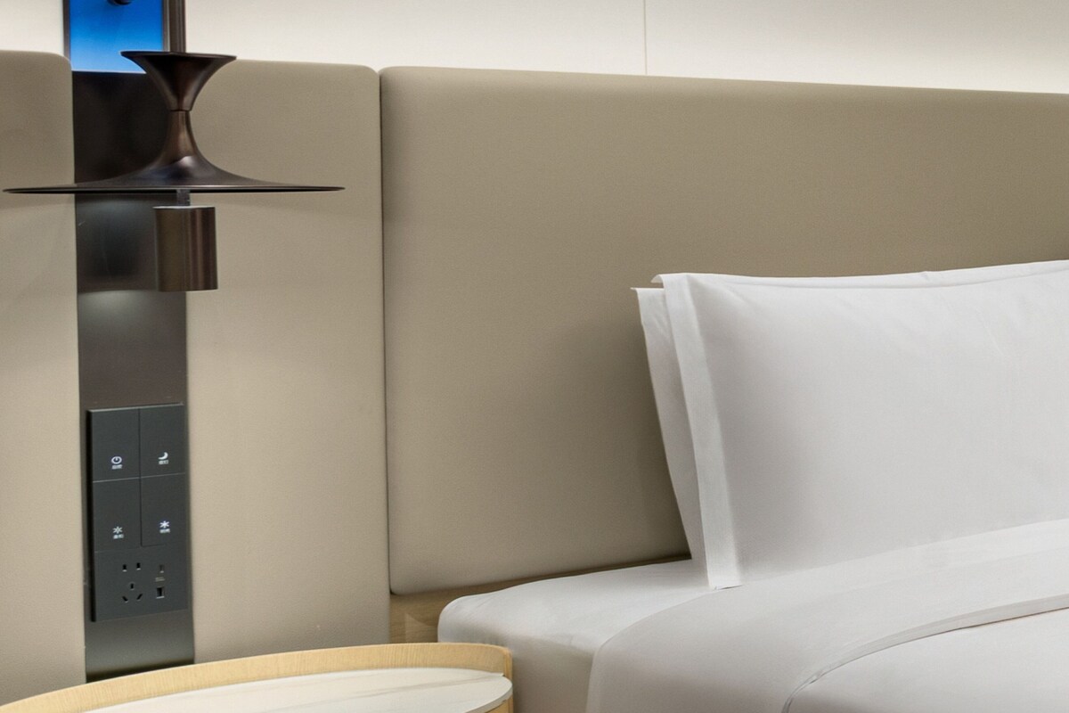 Una habitación de hotel moderna con una cama, un panel de control y una lámpara fijada a la pared.