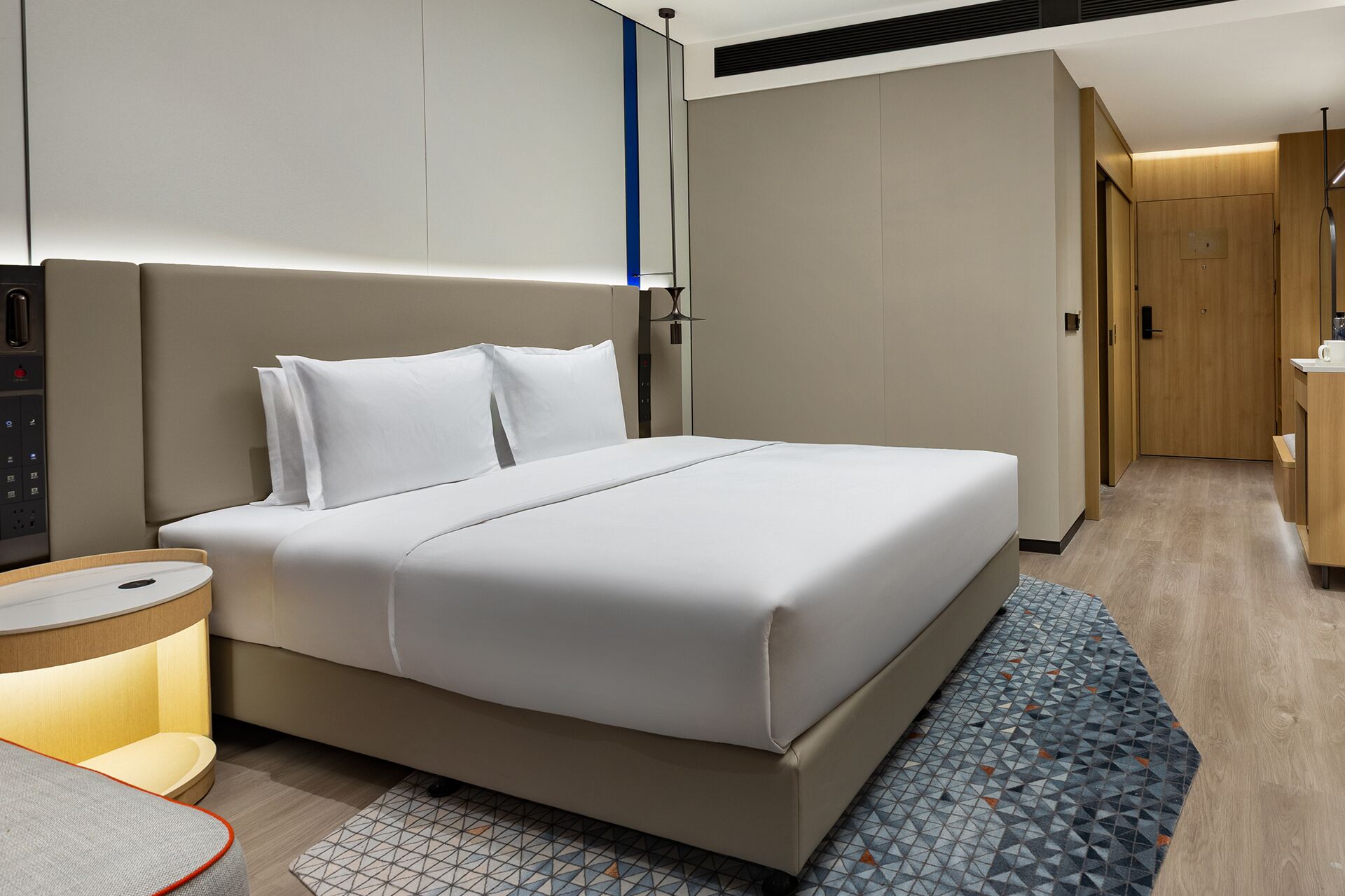 Moderni hotellihuone, jossa on suuri sänky, yöpöytä, työpöytä ja kylpyhuoneen ovi.