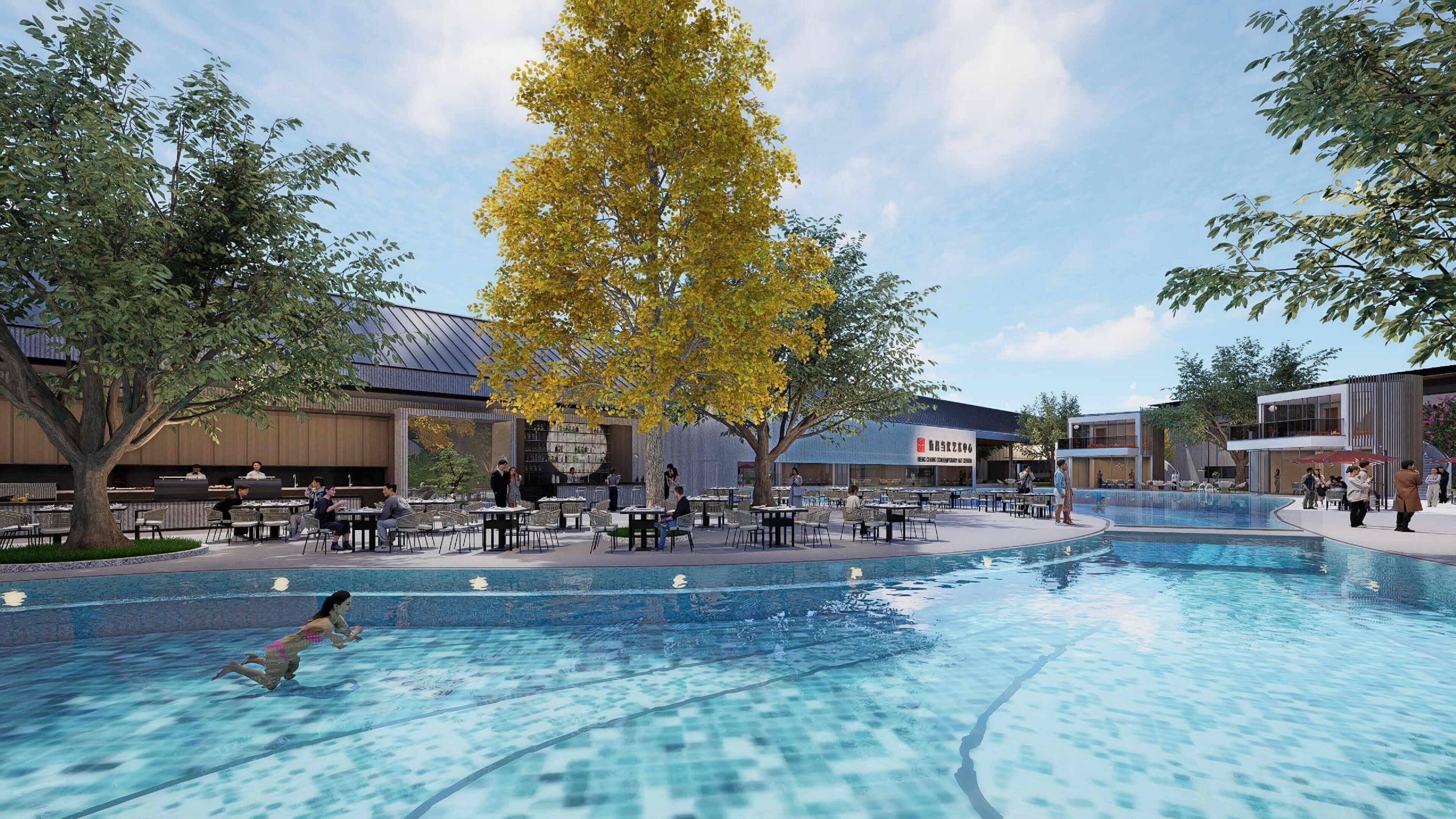 An outdoor pool area with tables and chairs, surrounded by trees and buildings.