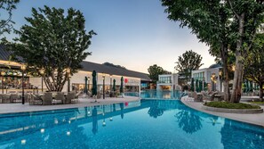 A swimming pool with lounge chairs and umbrellas, surrounded by trees and buildings with signage.