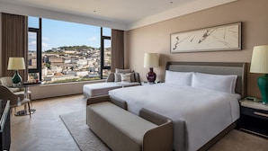 Een moderne hotelkamer met een groot bed, een bank, een bureau en uitzicht op een stadsbeeld.