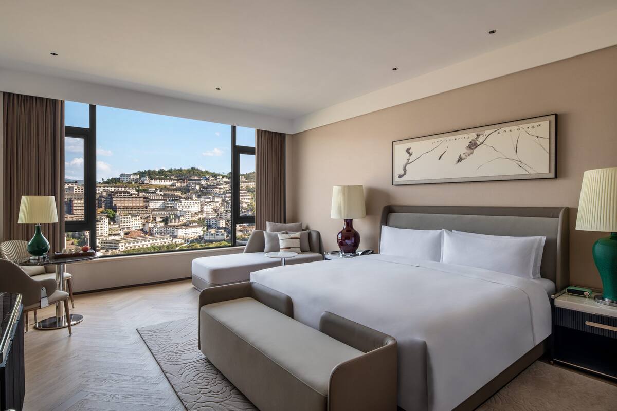 Ett modernt hotellrum med en stor säng, en soffa, ett skrivbord och utsikt över stadsbilden.