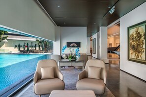 Un interior moderno con vistas a la piscina, dos sillones de cuero, una mesa de mármol y obras de arte en las paredes.