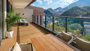 Een balkon met een houten vloer, rieten meubels en een potplant.