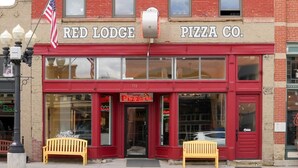 Red Lodge Pizza Co. -nimisen pizzerian myymälän julkisivu on punainen, sen edessä on kaksi penkkiä ja siinä on esillä Yhdysvaltain lippu.