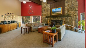 A spacious living room with a stone fireplace, a kitchen area with wooden cabinets, and a red accent wall. - Close to ski mountain, pool and hot tub (Red Lodge)