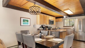 Une cuisine moderne avec des meubles en bois, un réfrigérateur en acier inoxydable et un coin repas comprenant une table en bois et des chaises grises.