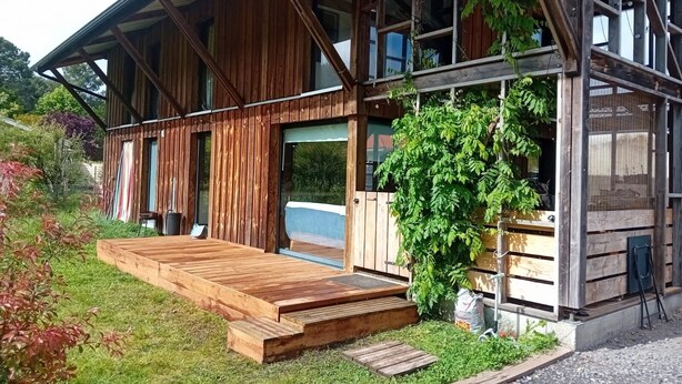Una cabaña de madera con terraza, ventanas grandes y un jardín.