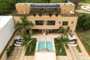 Un edificio moderno con terraza en la azotea, piscina y palmeras.