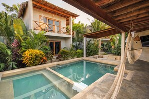 Une piscine entourée d’une terrasse en bois, d’un hamac et d’une végétation tropicale luxuriante.