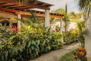 Un espace extérieur abrité, doté d’une pergola en bois, d’une végétation tropicale luxuriante et d’un chemin de gravier.