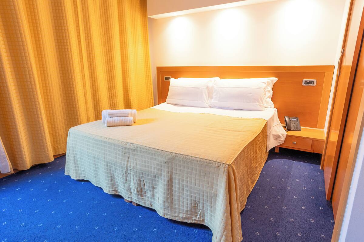 A hotel room with a bed, a nightstand, a telephone, and a curtain.