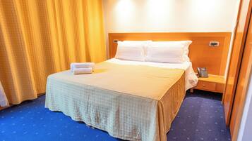 Quarto de hotel com cama, mesa de cabeceira, telefone e cortina.