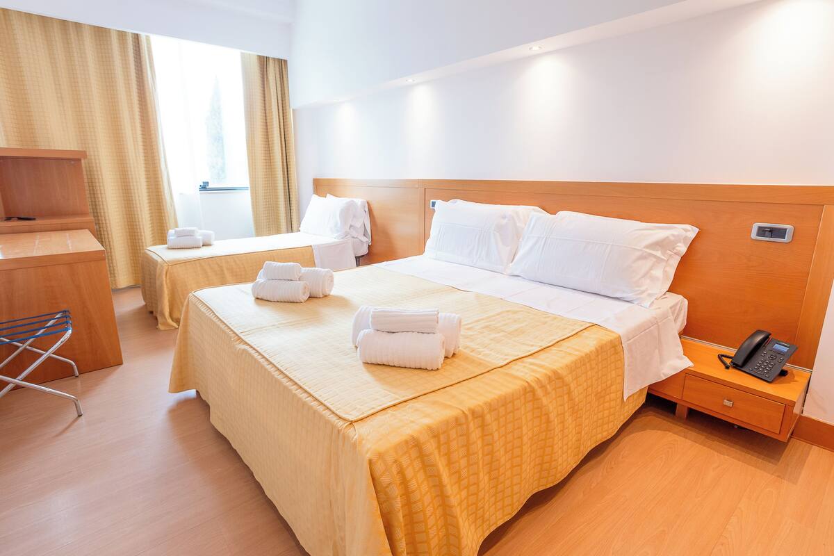 A hotel room with two beds, a desk, a chair, and a phone on a bedside table.