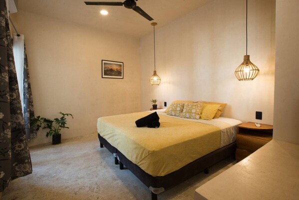 Une chambre à coucher comprenant un lit, deux tables de chevet, un ventilateur de plafond et deux lampes suspendues.