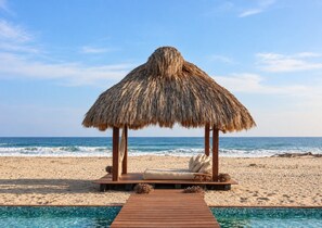 A beachside lounge with a thatched roof, a wooden deck, and a pool.