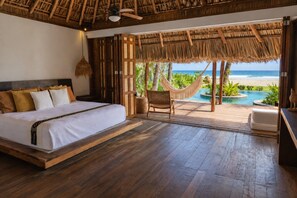 A bedroom with a bed, wooden flooring, a hammock, and a view of the ocean.