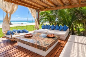A beachside lounge with a swing chair, a sofa with blue cushions, and a table with decorative shells.