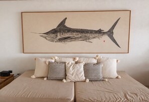Ein Bett mit Kopfteil, ein gerahmtes Kunstwerk darüber und ein Nachttisch mit Lampe.