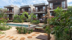 Ein modernes Resort mit mehreren zweistöckigen Gebäuden, einem Schwimmbad und einem gepflegten Garten mit verschiedenen Pflanzen und Holzliegen.