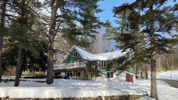 Ein zweigeschossiges Haus mit Steinfundament, umgeben von Bäumen und bedeckt mit Schnee.