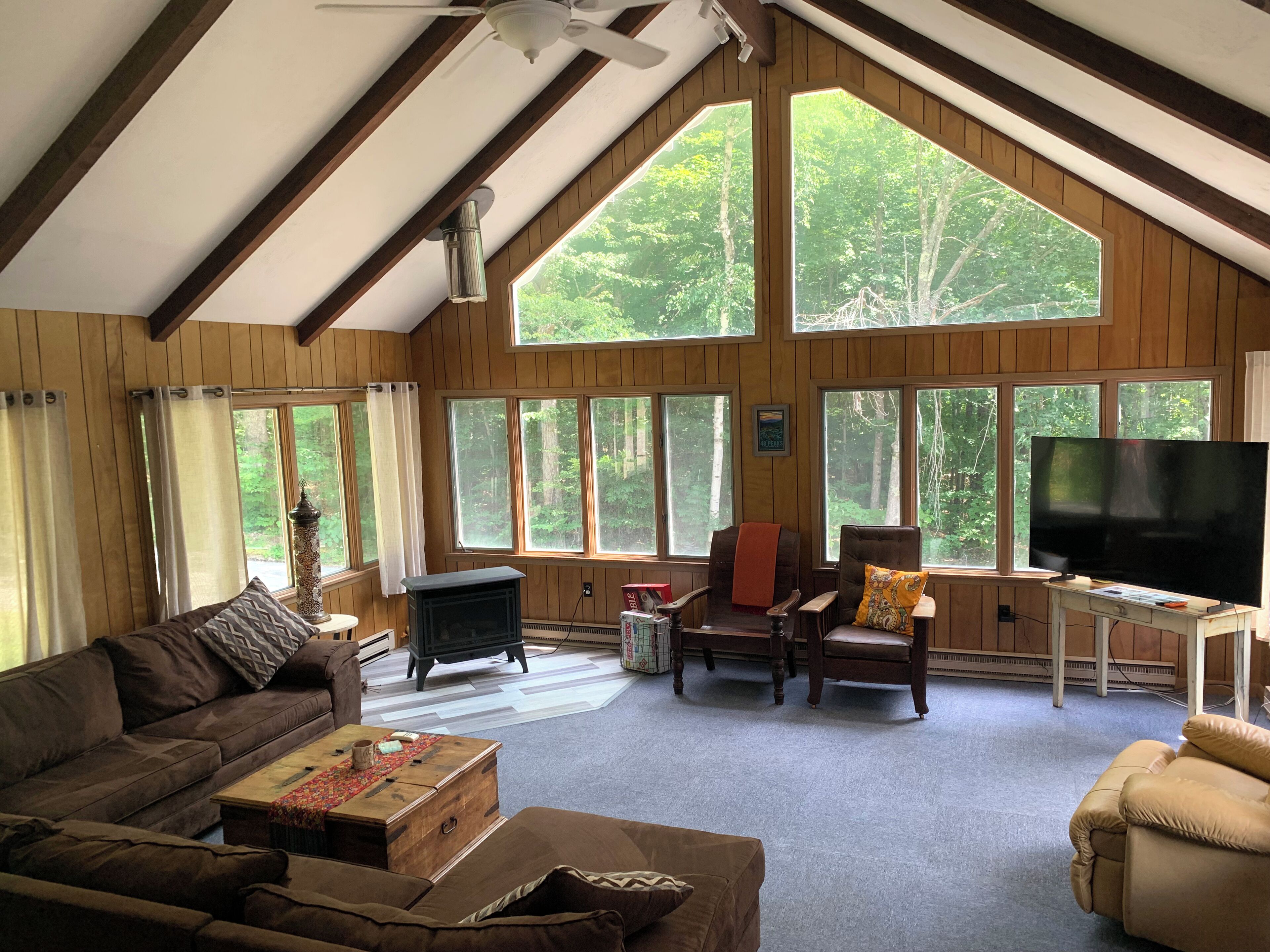 A cozy living room with a fireplace, comfortable seating, and large windows offering a view of the forest.