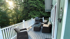 Eine Terrasse mit Korbmöbeln und einem Grill, umgeben von weißen Geländern und viel Grün.
