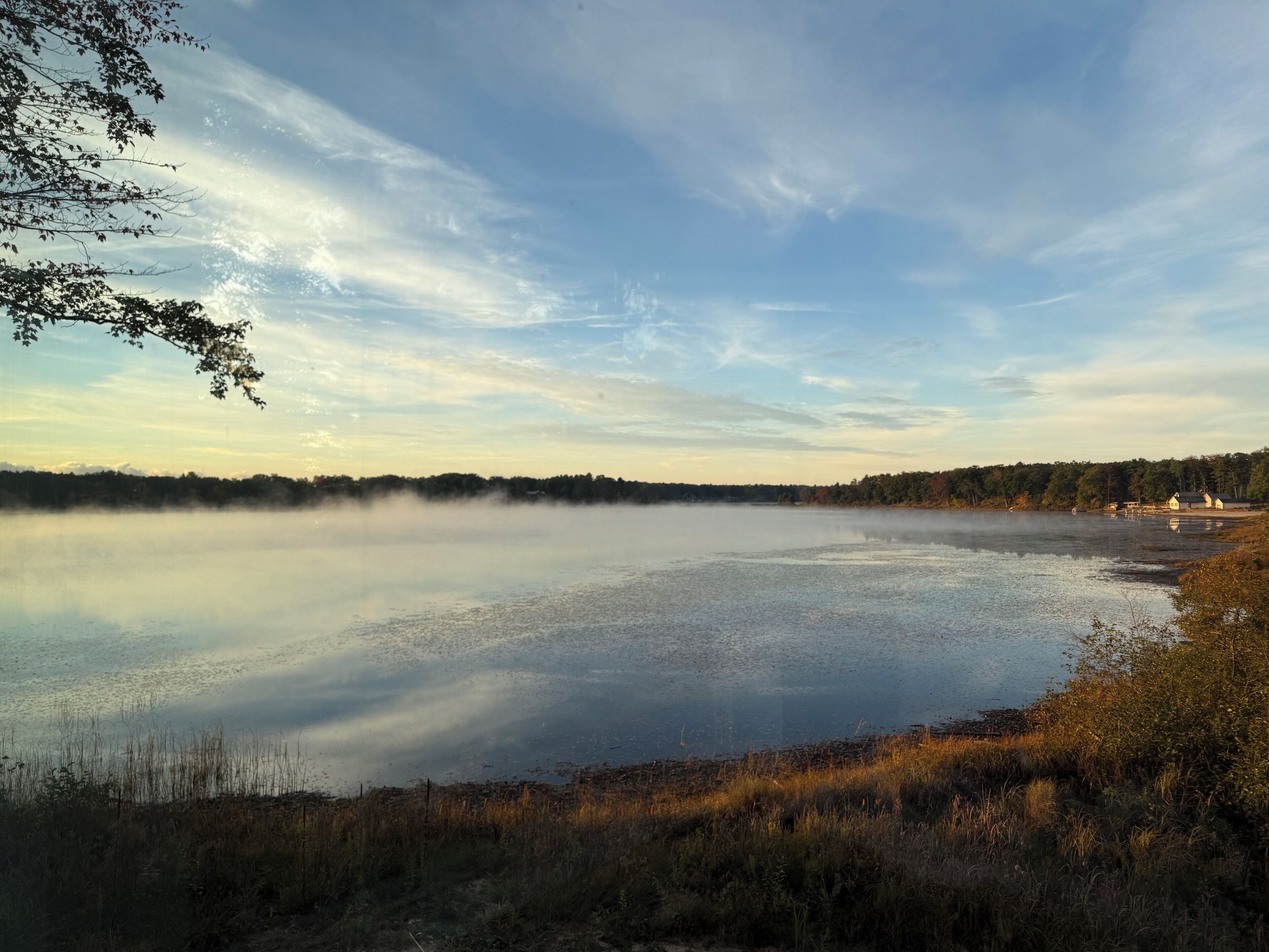 A calm lake with a forested shoreline and a few buildings in the distance.