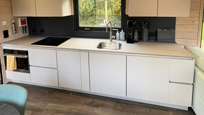 Eine moderne Küche mit weißen Schränken, einer schwarzen Arbeitsplatte und einem Fenster mit Blick auf Grünflächen.