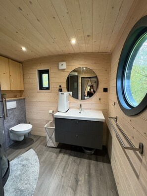 Une salle de bain moderne avec des murs en bois, un miroir rond, un lavabo et des toilettes.