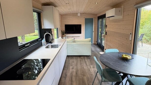 Eine moderne Küche mit Holzboden, eingebauten Geräten und einem Essbereich mit rundem Tisch und Stühlen.