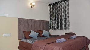 Een slaapkamer met een houten hoofdbord, een bed met bruin en blauw beddengoed en een kamerbreed gordijn met dessin.