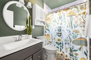 Un baño con lavamanos blanco, inodoro, espejo y cortina de ducha con estampado floral.