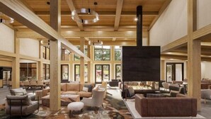 Un hall d’entrée spacieux avec de hauts plafonds, des poutres en bois et de grandes fenêtres. On y trouve une cheminée et des coins salon confortables.