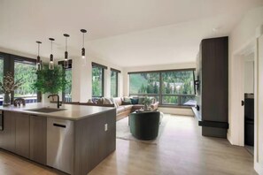 A modern kitchen with a central island, a dining area with a sofa, and large windows offering a view of greenery. - Kindred Resort Luxury Ski In, Ski Out 3 Bedroom Residence at the River Run Gondola (Keystone)