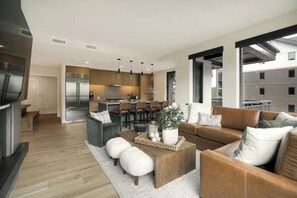 A modern living room with a sofa, ottomans, and a coffee table. There is a kitchen in the background with a dining area. - Kindred Resort Luxury Ski In, Ski Out 3 Bedroom Residence at the River Run Gondola (Keystone)