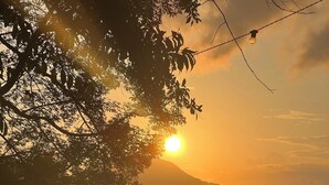 A sunset view with a boat on the water, a table with a drink, and a person sitting at the table. - Pousada Três Coqueiros (Angra dos Reis)