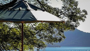A wooden deck with a table and chairs, overlooking a body of water with a mountain in the background. - Pousada Três Coqueiros (Angra dos Reis)