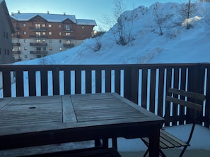 A wooden deck with a table and chairs, overlooking a snow-covered slope and a building with balconies. - Apartment Puy st Vincent 1800, 35 m2, 3 rooms, sleeps 6, covered swimming pool (Puy-Saint-Vincent)