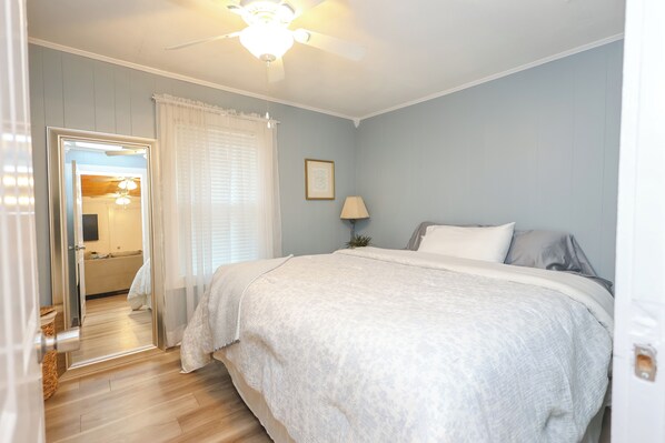 Un dormitorio con una cama, un ventilador de techo, una mesita de noche con una lámpara y un cuadro en la pared.