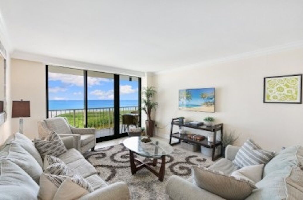 A living room with a large window, a sofa set, a coffee table, and a bookshelf.