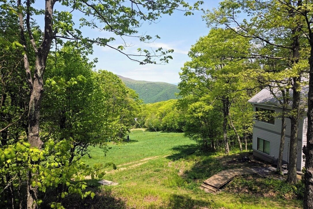 Une cabane offrant une vue sur un champ verdoyant et sur des collines à l’horizon.