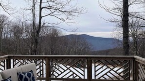 A deck with a sofa and cushions, overlooking a snowy landscape with trees and distant hills.