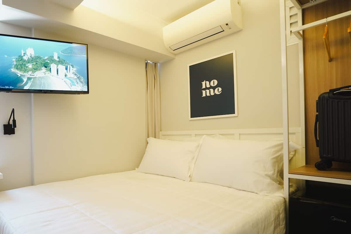 Une chambre d’hôtel équipée d’un lit, d’un téléviseur fixé au mur, d’un appareil de climatisation et d’un tableau encadré avec une inscription.