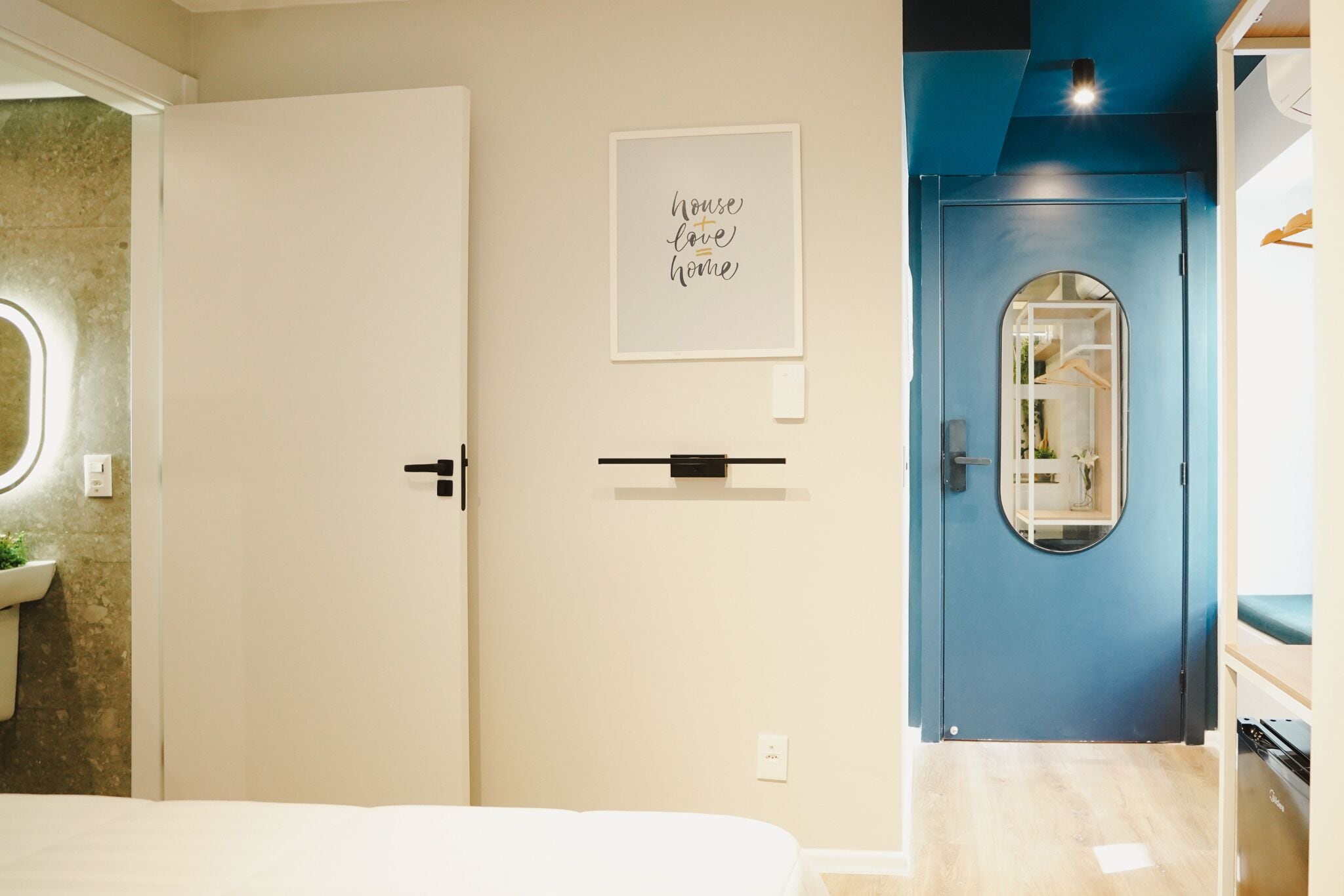 A bedroom with a bed, a door with a mirror, a framed quote on the wall, and a blue door leading to another room.