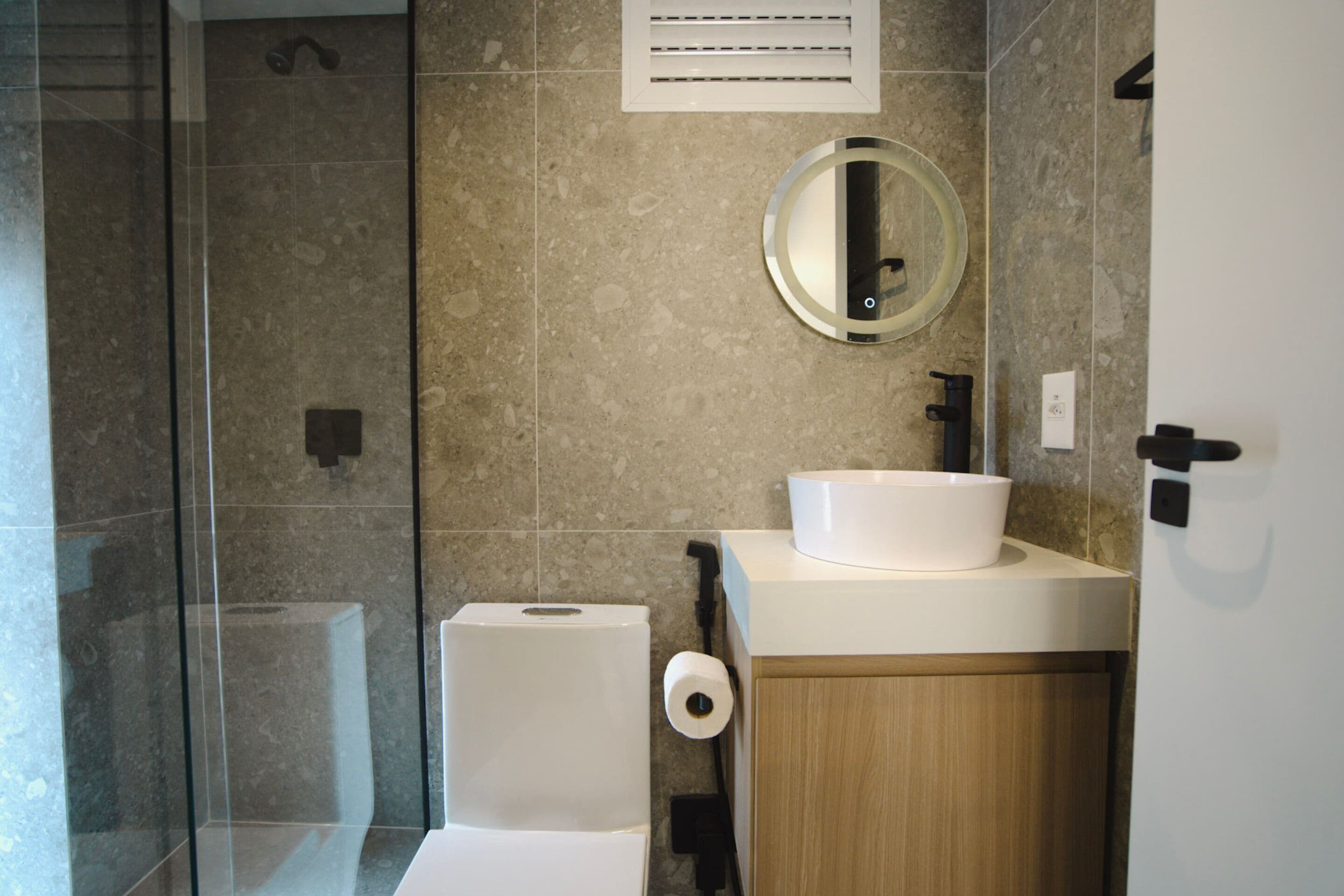 Un baño moderno con ducha envuelta en vidrio, inodoro, lavamanos con espejo y un perchero para toallas.