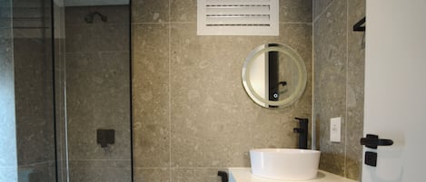 A modern bathroom with a glass-enclosed shower, a toilet, a sink with a mirror above it, and a towel rack.